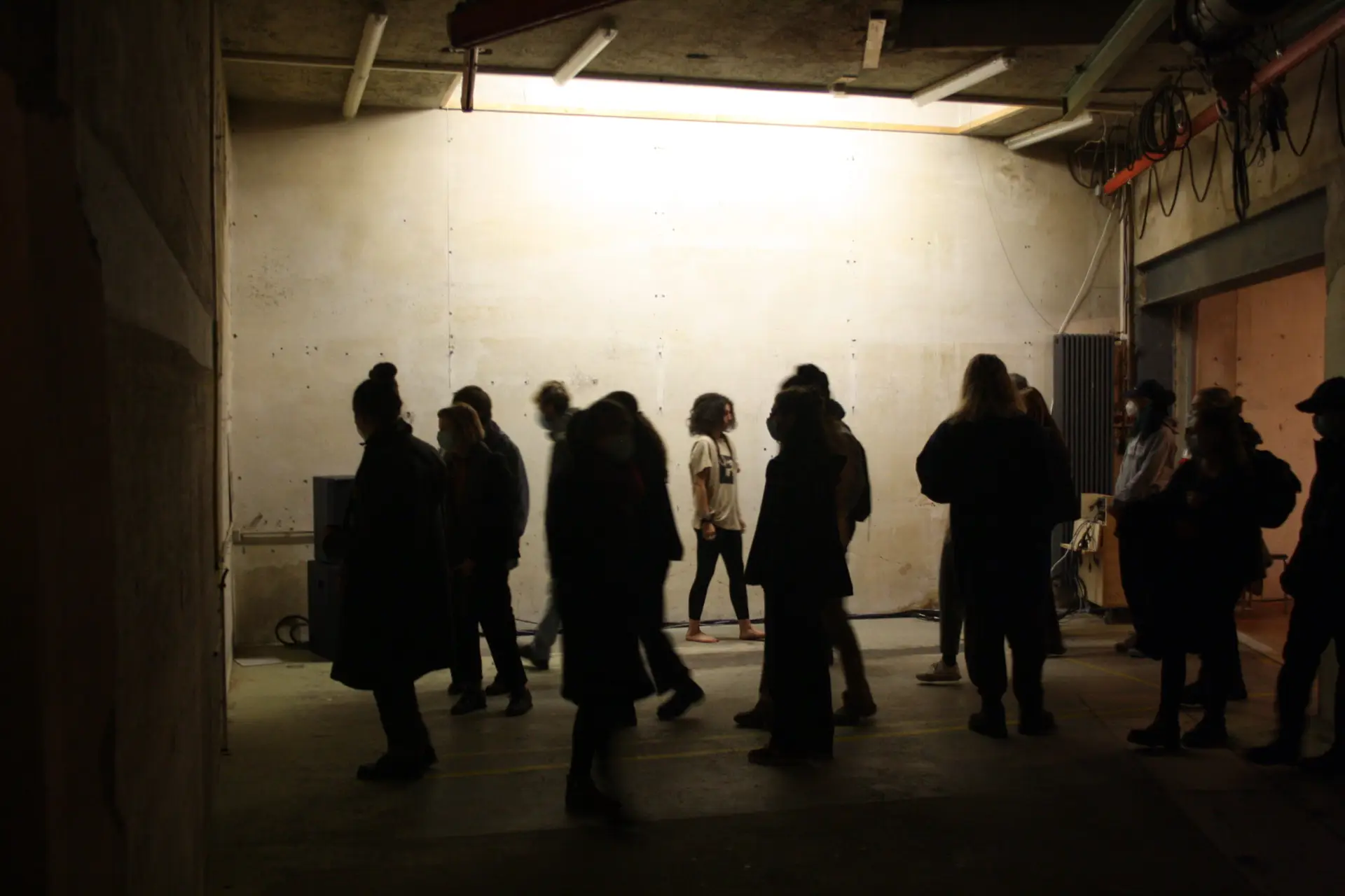 PORTRÄTS MEINES VATERS (2021): audience silhouetted in a dim basement against a brightly lit wall