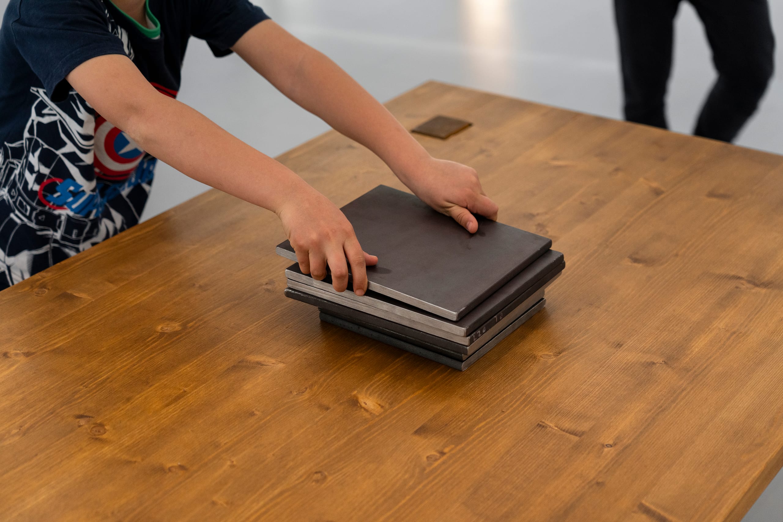 ARCHETYPAL COLLAPSE (2022): a child stacking metal weight plates on the wooden tabletop