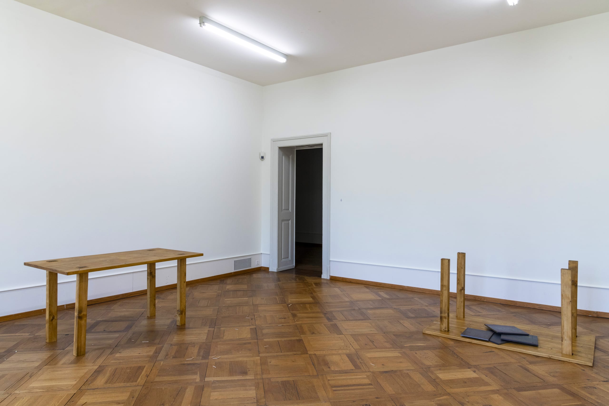 ARCHETYPAL COLLAPSE (2022): a standing table and a collapsed one with weights on its fallen top, on parquet