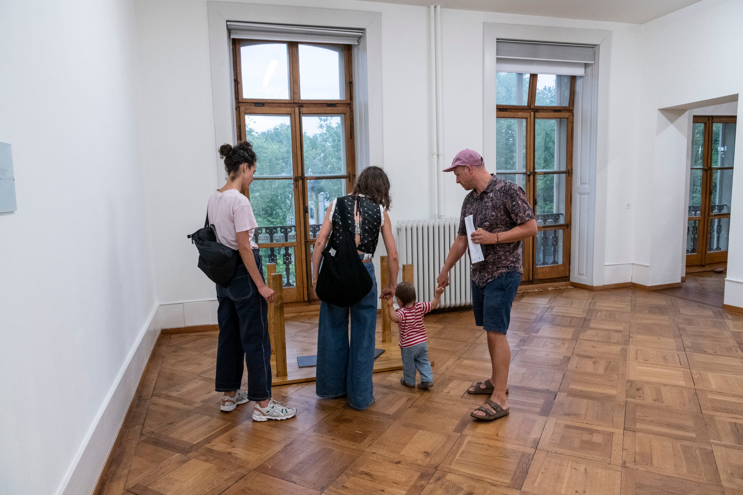 ARCHETYPAL COLLAPSE (2022): visitors and a small child around a collapsed table in a room with tall windows
