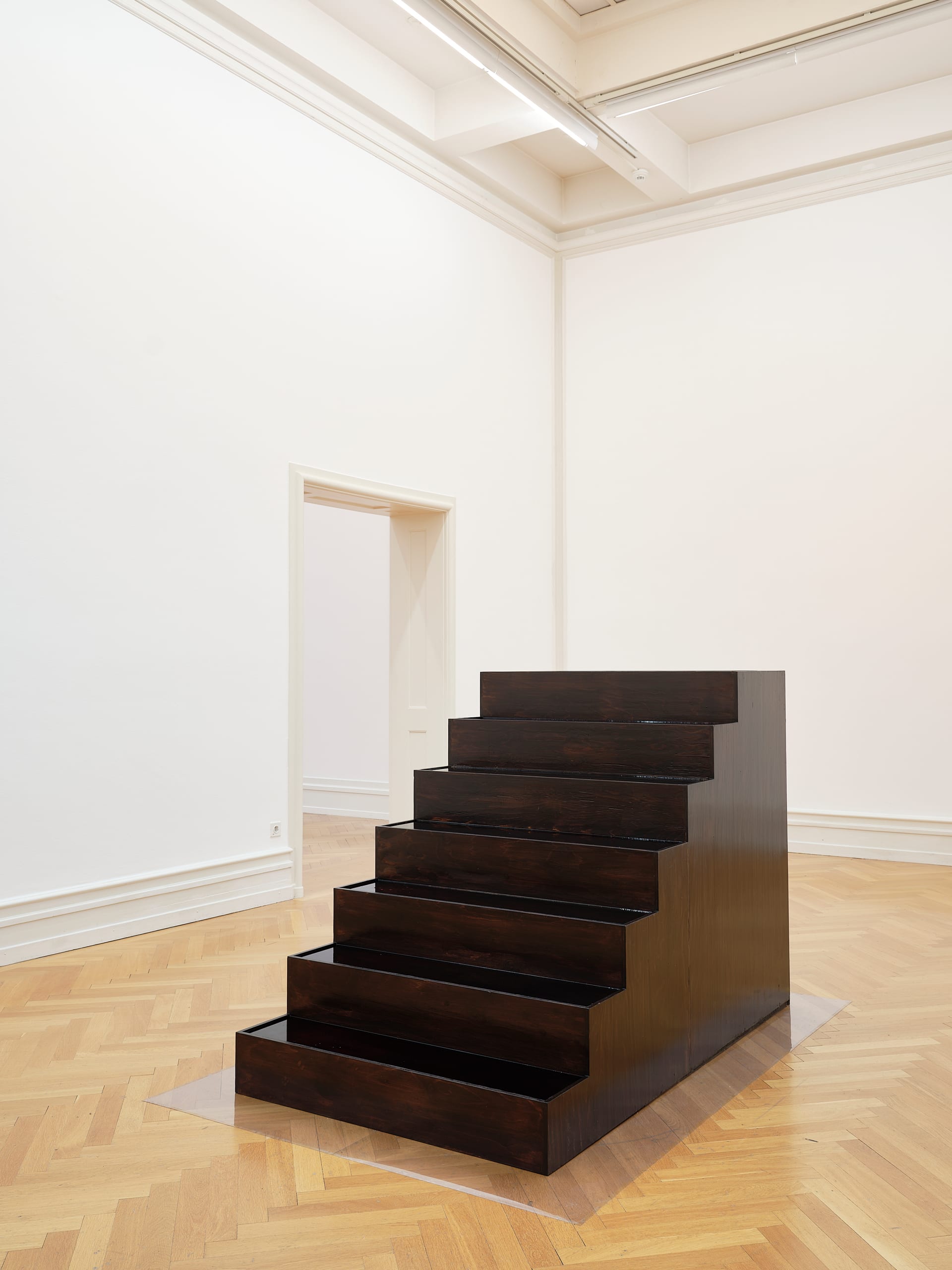 CENTO GIORNI D’ACETO (2020): dark wooden stepped sculpture on a herringbone parquet floor in a white gallery