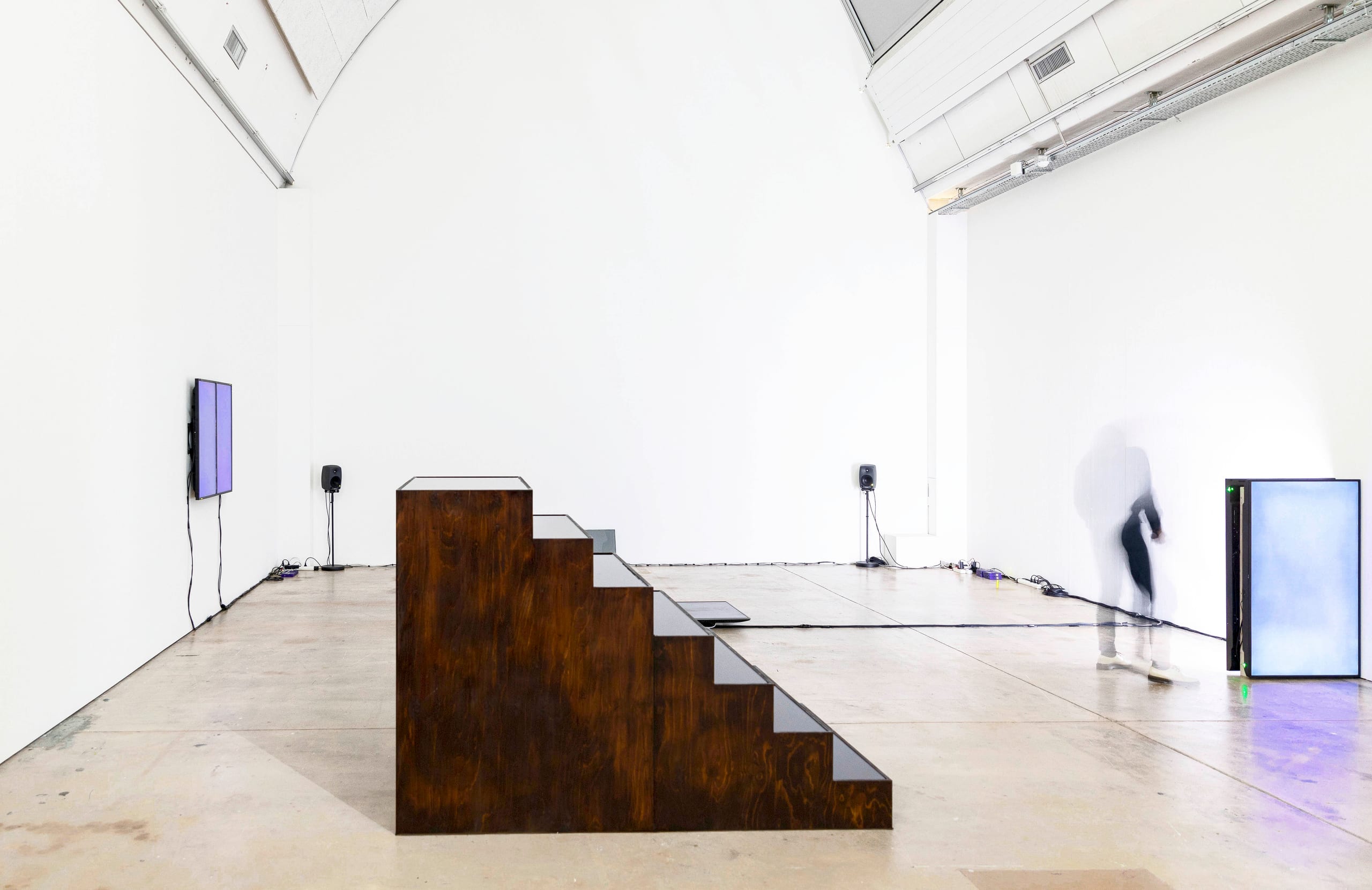 CENTO GIORNI D’ACETO (2020): dark wooden stepped sculpture in a large white exhibition hall