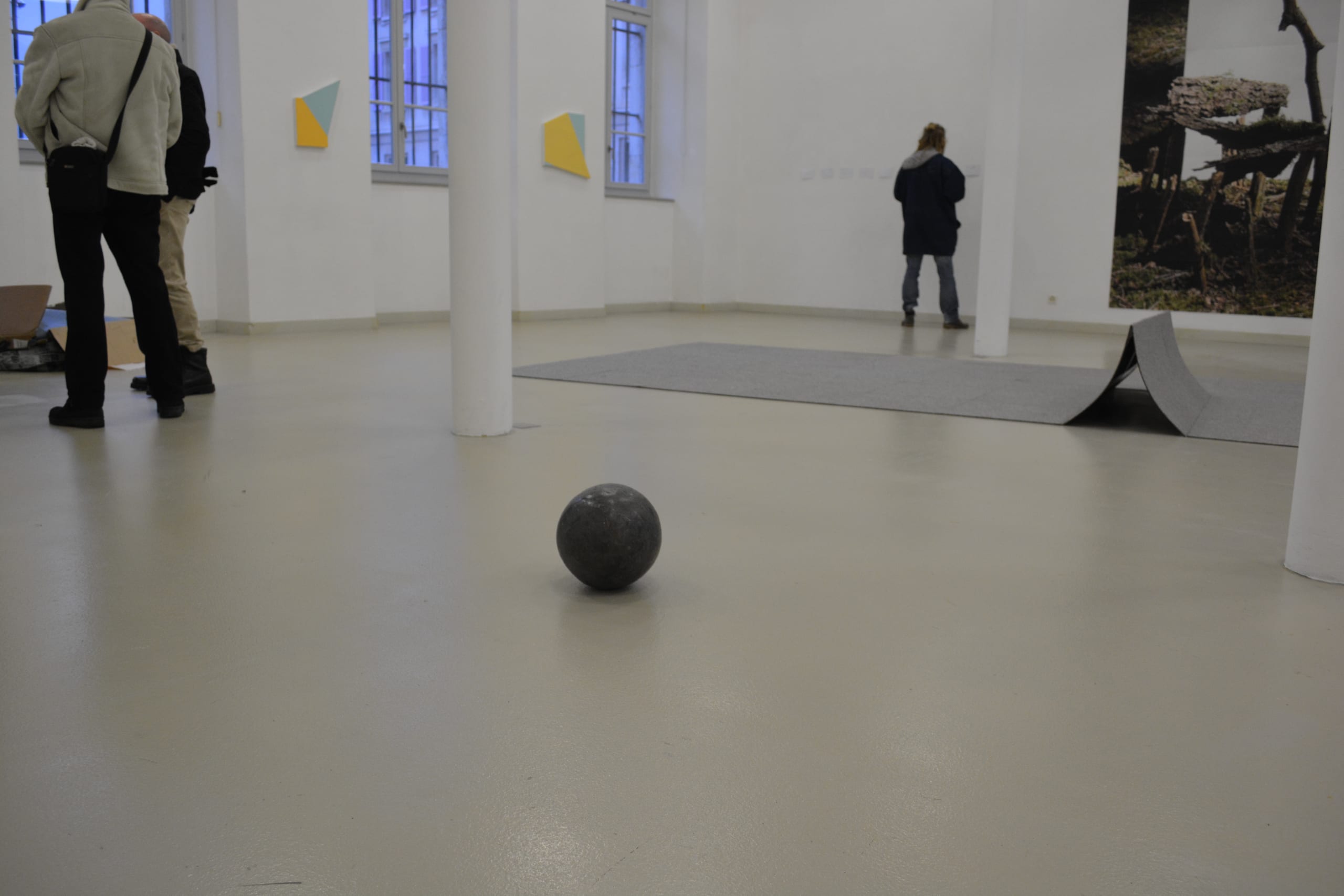 L’equivalente del mio peso in piombo (2023): lead ball on the floor of a white gallery with visitors