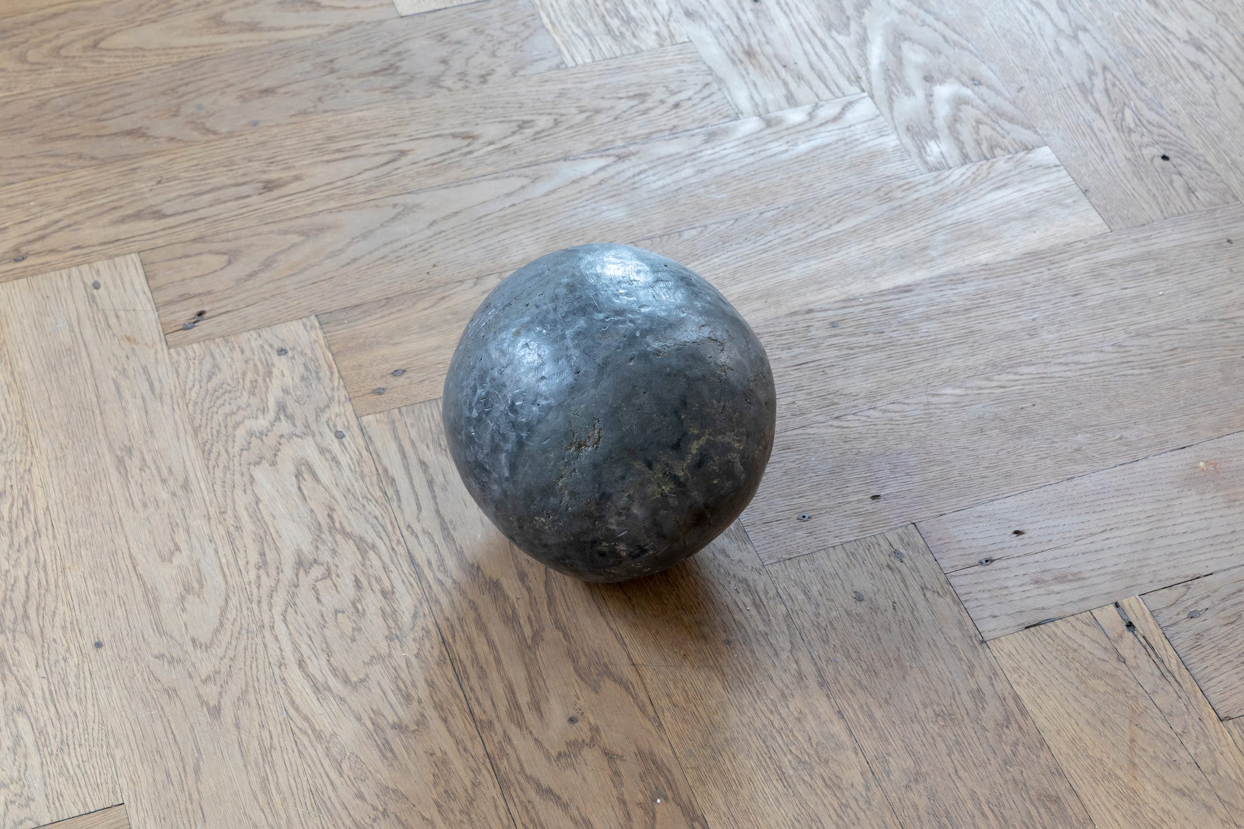 L’equivalente del mio peso in piombo (2023): lead ball on a herringbone parquet floor
