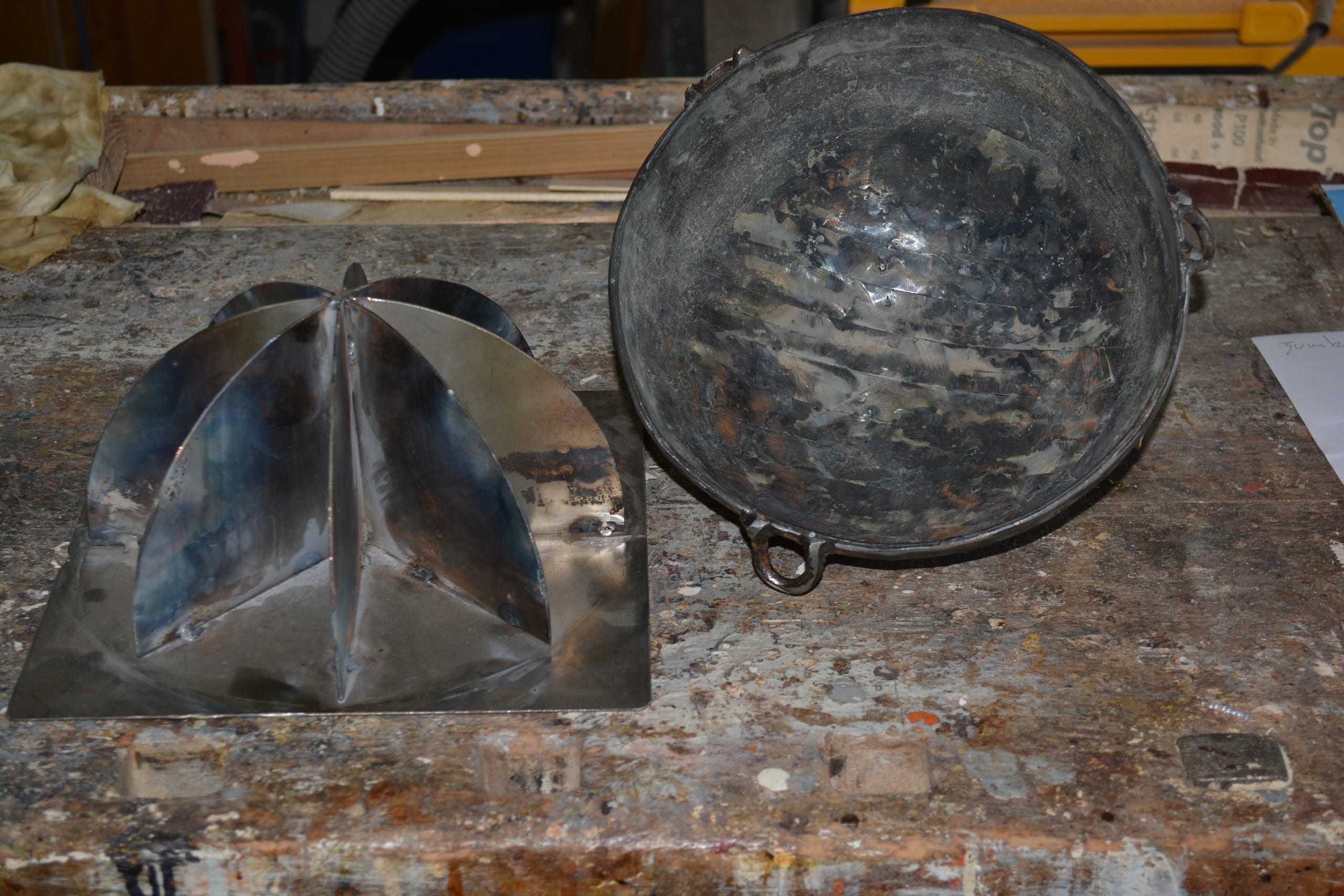 L’equivalente del mio peso in piombo (2023): sheet-metal form and a round metal bowl on a paint-stained workbench