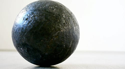 L’equivalente del mio peso in piombo (2023): dark lead ball on a pale floor against a white wall