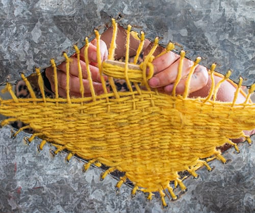 Manta de Carnaval (2024): hands weaving yellow wool through holes in an engraved zinc sheet