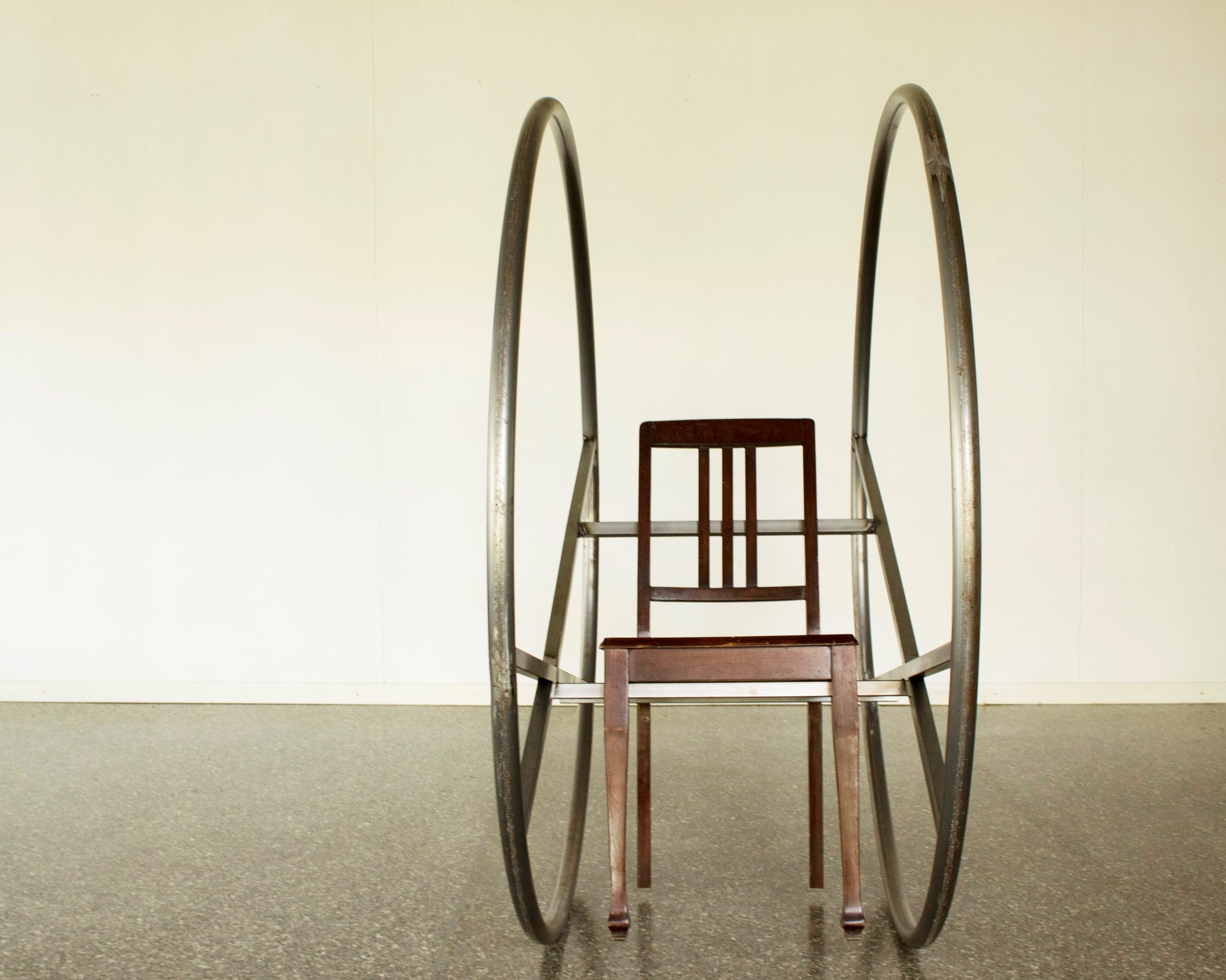 wave chair (2021): wooden chair mounted between two large iron rings, front view